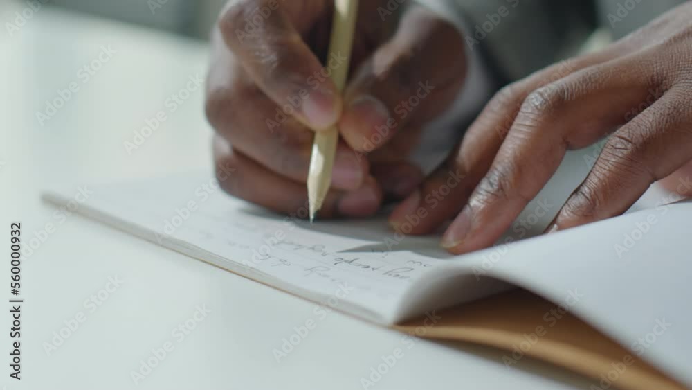 Close up shot of hands of black businessman writing down some notes with pencil in copybook Close up shot of hands of black businessman writing down some notes with pencil in copybook