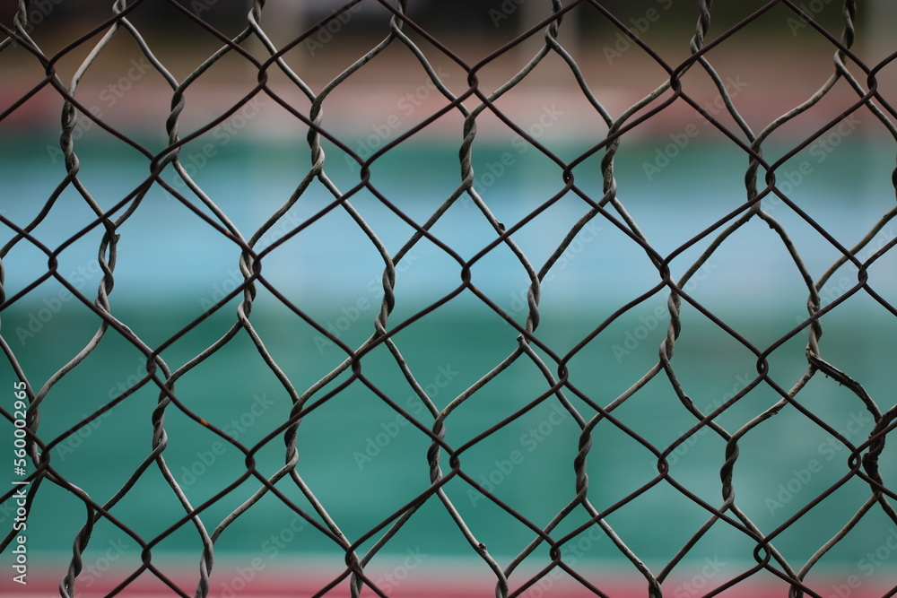 Fototapeta premium This image shows a chainlink fence surrounding a courtyard. The fence is made of metal links that are connected together to form a tall wall.