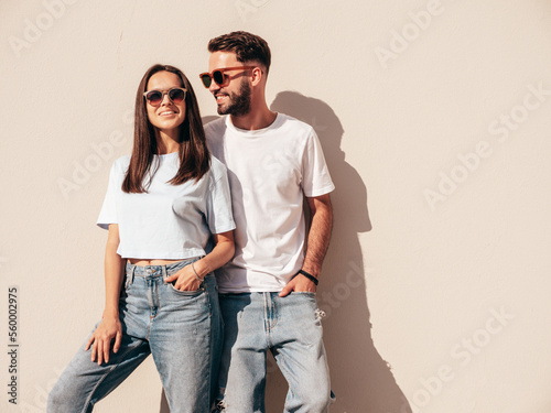 Smiling beautiful woman and her handsome boyfriend. Woman in casual summer jeans clothes. Happy cheerful family. Female having fun. Sexy couple posing in the street at sunny day. Near white wall