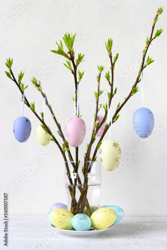 Painted Easter eggs hang on branches on white wooden table