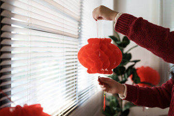 Asian woman wearing red clothes making paper craft red Chinese new year lantern for Lunar New Year decorations Chinese New Year Celebrations for good luck.