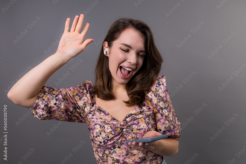 An emotional young woman dances on a gray background in the studio. The model listens to music with headphones An emotional young woman dances on a gray background in the studio. The model listens to music with headphones