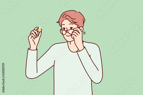 Positive man examines gold coin or piece of jewelry and lowers glasses from eyes to view rare exhibit. Guy is fond of numismatics and collecting coins from precious metals. Flat vector design 