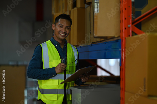 Smiling asian male warehouse worker checking goods and supplies on shelves in large warehouse
