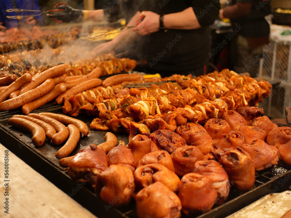 Slightly blurred pork knuckles, skewers and sausages on a huge grill, on the Krakow christmas market.