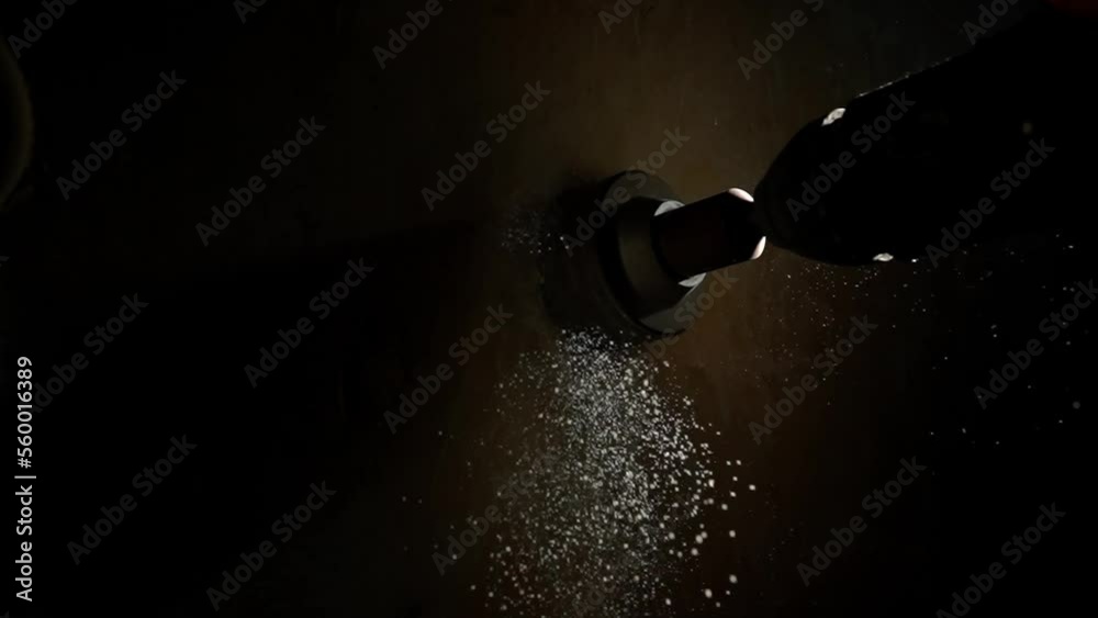 Macro shot of drilling round hole for socket on wall in dark with light beam. Metal round nozzle cup rotating on electric drill or perforator. In process of drilling white dust from plaster crumbles.