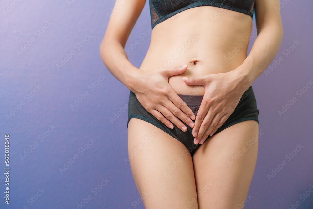 Close-up woman in underwear holds her hands to her lower abdomen, purple background. gynecology and women health concept.