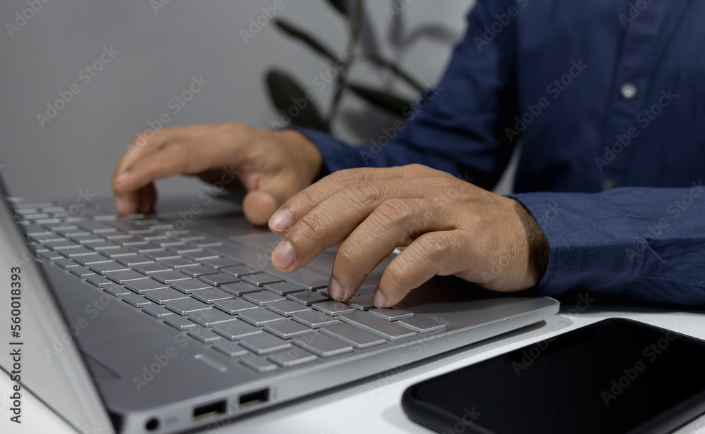 Man using laptop at home while sitting at wooden table, male hands typing on notebook keyboard, concept of young people working mobile phone working online Man using laptop at home while sitting at wooden table, male hands typing on notebook keyboard, concept of young people working mobile phone working online