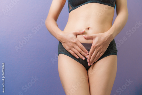 Close-up woman in underwear holds her hands to her lower abdomen, purple background. gynecology and women health concept. © NanSan