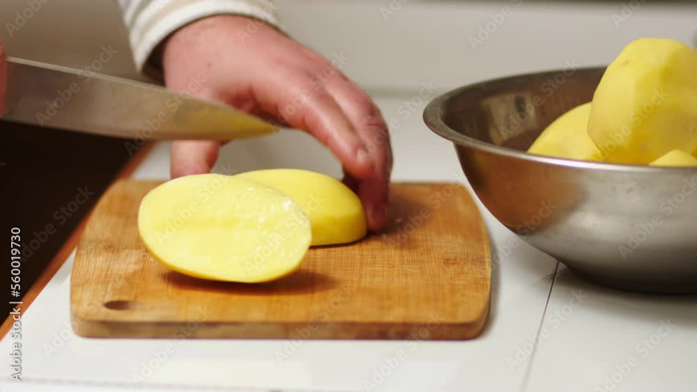 Male cook cuts raw potatoes for cooking vegetable food, cuts potatoes on a wooden cutting board, the hostess prepares food in her kitchen, a delicious dish for a vegetarian Male cook cuts raw potatoes for cooking vegetable food, cuts potatoes on a wooden cutting board, the hostess prepares food in her kitchen, a delicious dish for a vegetarian