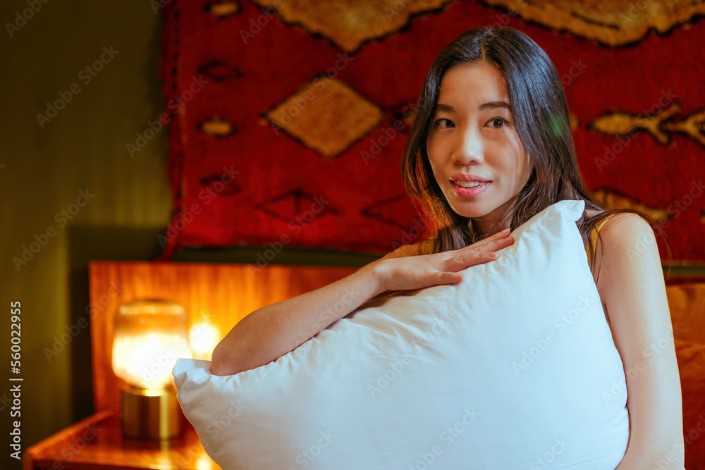 Vietnamese woman hugging the pillow looking away in bedroom