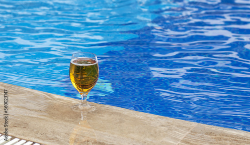 glass with fresh cold beer on pool edge blue color water waves mockup free space for text copy paste.vacation time mood travel all inclusive hotel trip relax on lounger sea beach  #560023147
