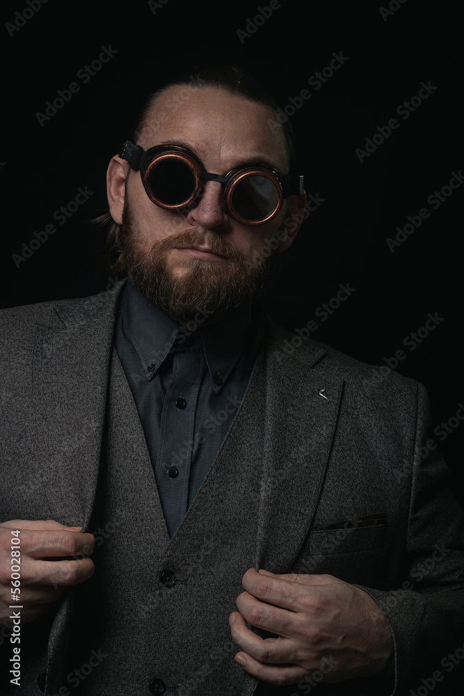 Obraz premium charismatic man in a classic suit and steampunk goggles on a black background stylish Portrait