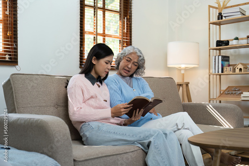 Loving adult daughter hugging older mother on couch at home, family enjoying tender moment together, young woman and mature mum or grandmother looking at each other, two generations.