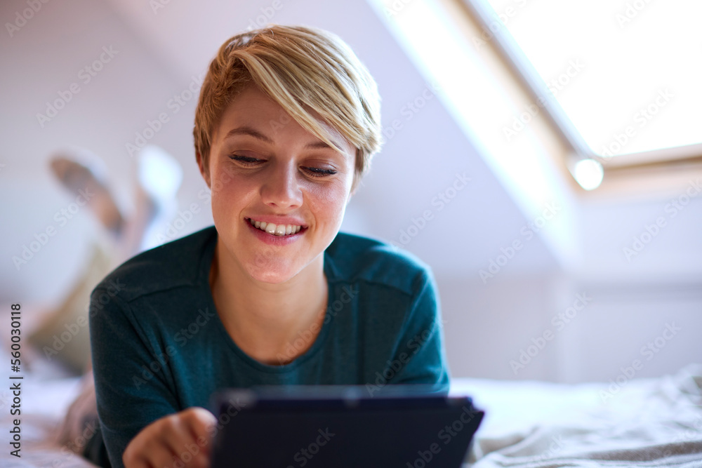 Young Smiling Woman Lying On Bed Wearing Pyjamas At Home Looking At Digital Tablet Young Smiling Woman Lying On Bed Wearing Pyjamas At Home Looking At Digital Tablet