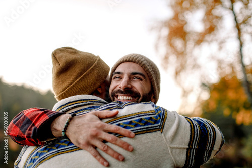 Young man embracing happy male friend wearing knit hat