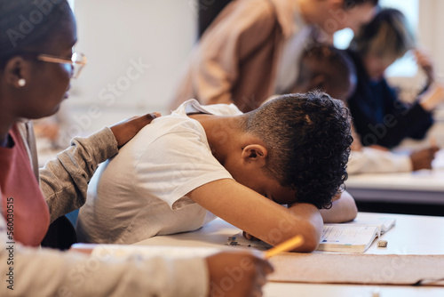 Female student consoling depressed teenage boy resting head on desk in classroom