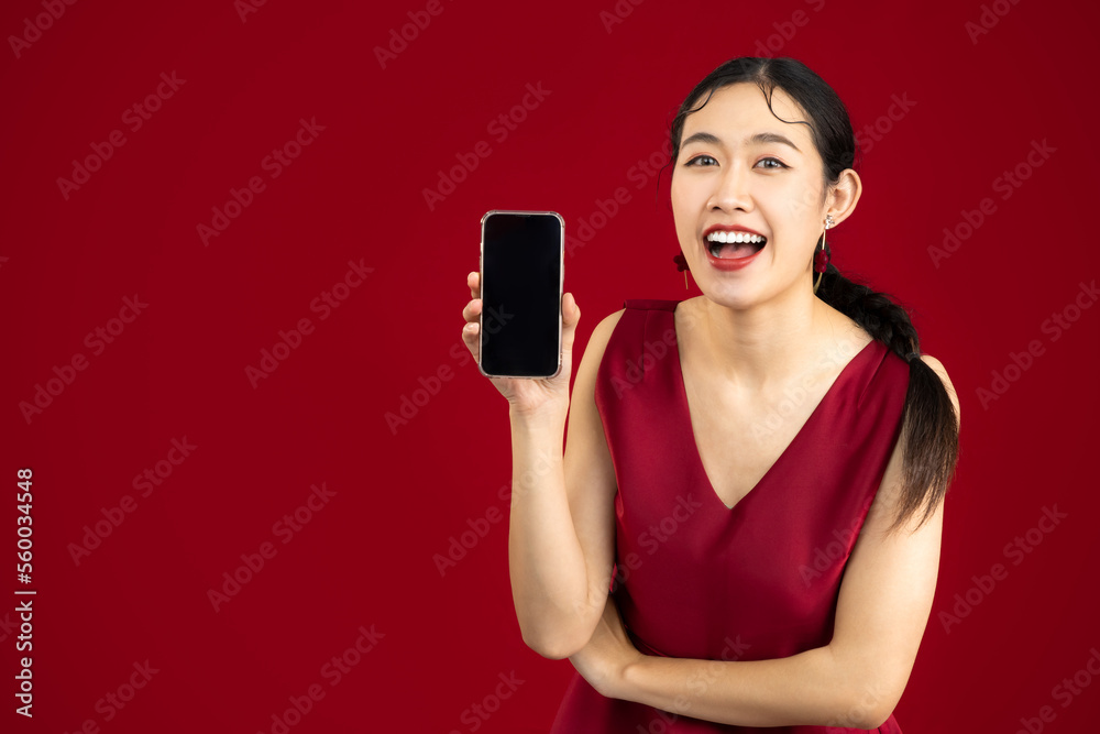 Young beautiful asian woman wear elegant red dress holding and showing blank screen smartphone on red color background. Young beautiful asian woman wear elegant red dress holding and showing blank screen smartphone on red color background.