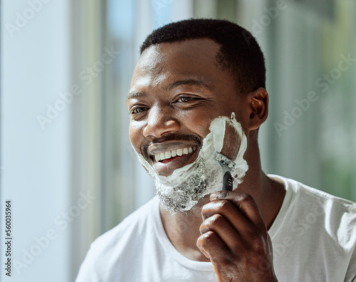 Face, shaving and razor with a black man grooming in the bathroom mirror of his home for beauty or skincare. Beard, shave and blade with a handsome male in the morning for his hair removal routine