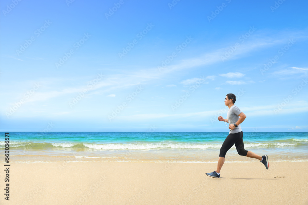Asian man jogging  on tropical sandy beach with blue sea and clear sky background.