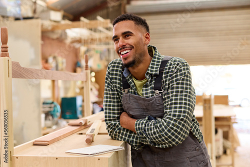 Portrait Of Male Apprentice Working As Carpenter In Furniture Workshop 