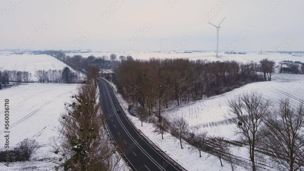 Alone black car hatchback driving on countryside road near snowy forest with windmills turbines on background. Automobile traveling lifestyle and journey concept Alone black car hatchback driving on countryside road near snowy forest with windmills turbines on background. Automobile traveling lifestyle and journey concept