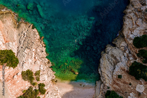 The girl swims to the shore in the azure sea between the rocks. Drone shot top view. High quality photo