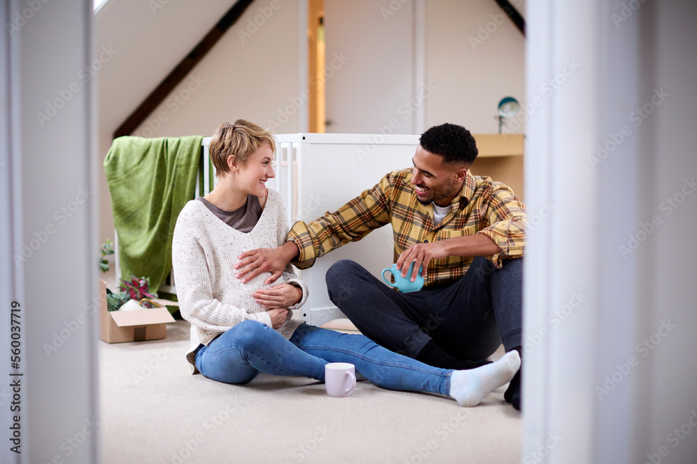 Couple Expecting Baby Relaxing In Nursery Of New Home Together With Moving In Boxes