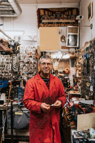Portrait of smiling mature male locksmith wearing red coat in workshop photo