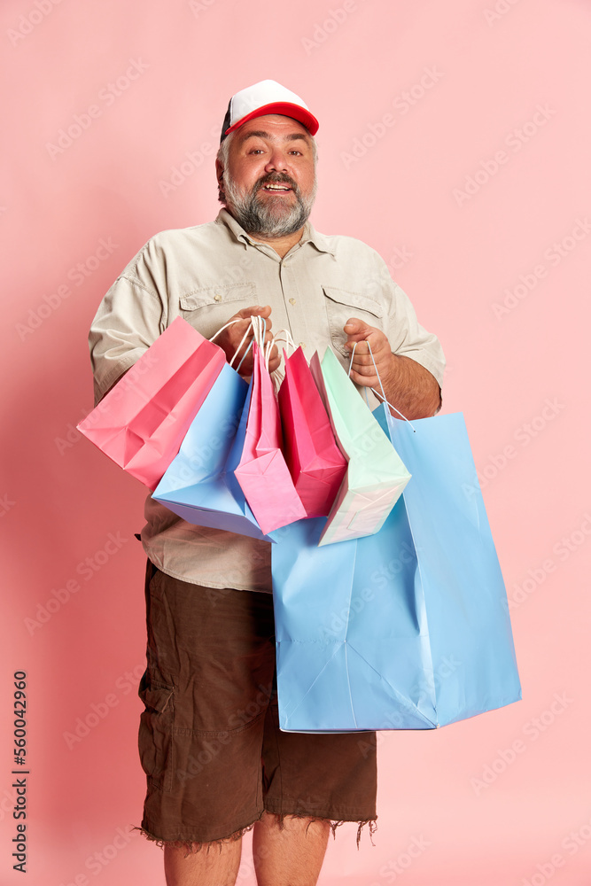 Portrait of mature man in casual clothes going shopping, posing with shopping trolley over pink studio background. Bying presents Portrait of mature man in casual clothes going shopping, posing with shopping trolley over pink studio background. Bying presents