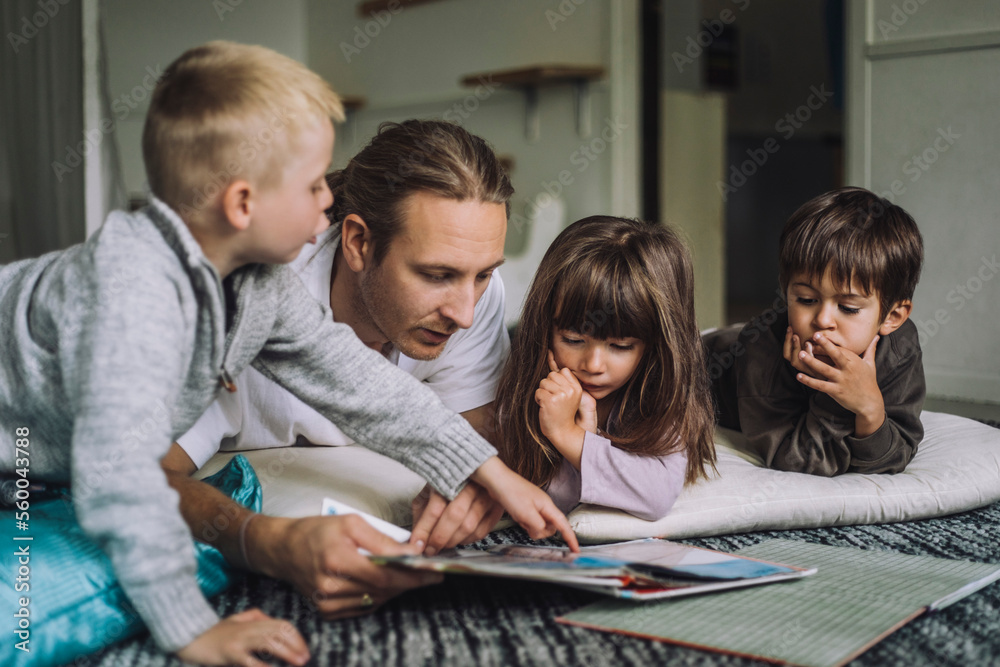 Male child care worker reading story book to students in kindergarten Male child care worker reading story book to students in kindergarten