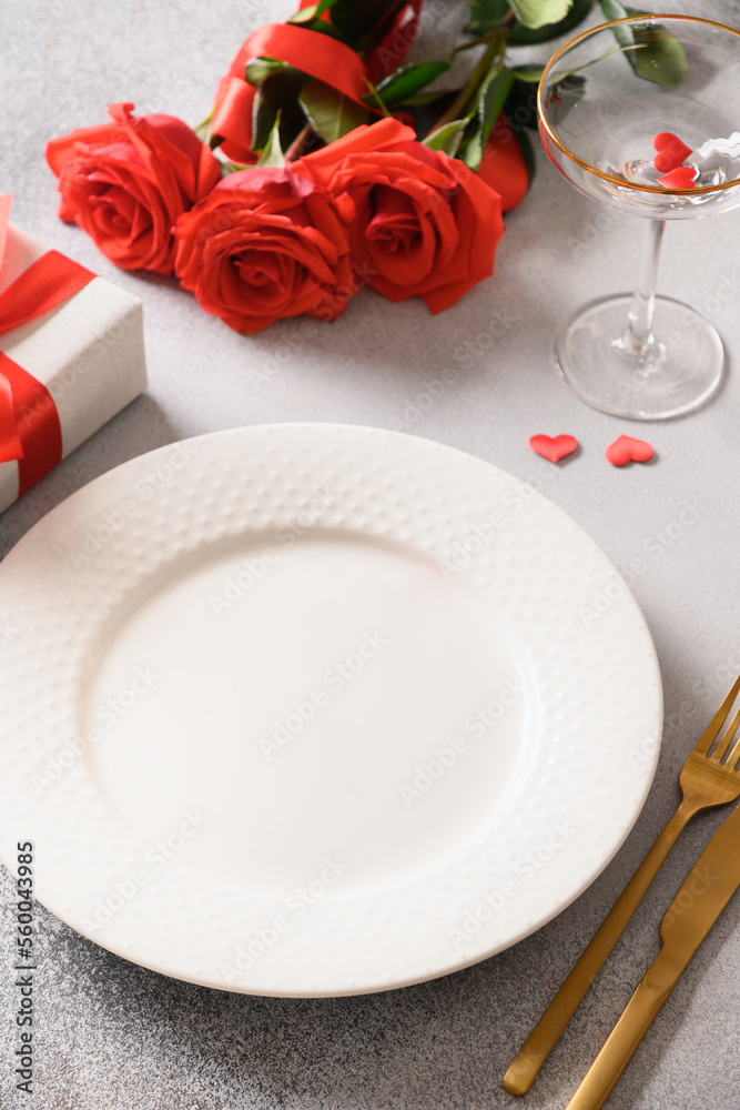 Valentine's day dinner with romantic gift, wine and red roses on gray background. Close up. Vertical format.