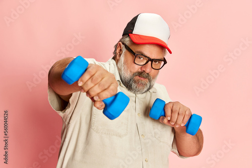 Portrait of overweight young woman posing with dumbbells over yellow studio background