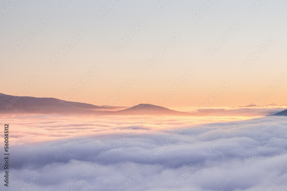 View of sea of clouds colored in the soft orange-pink hue of the morning sun. Peaks of the mountains rising out of this impermeable curtain. Sense of immortality and bliss. Beskydy, Czech republic