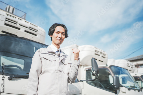 トラックの前でガッツポーズをする若い男性ドライバー