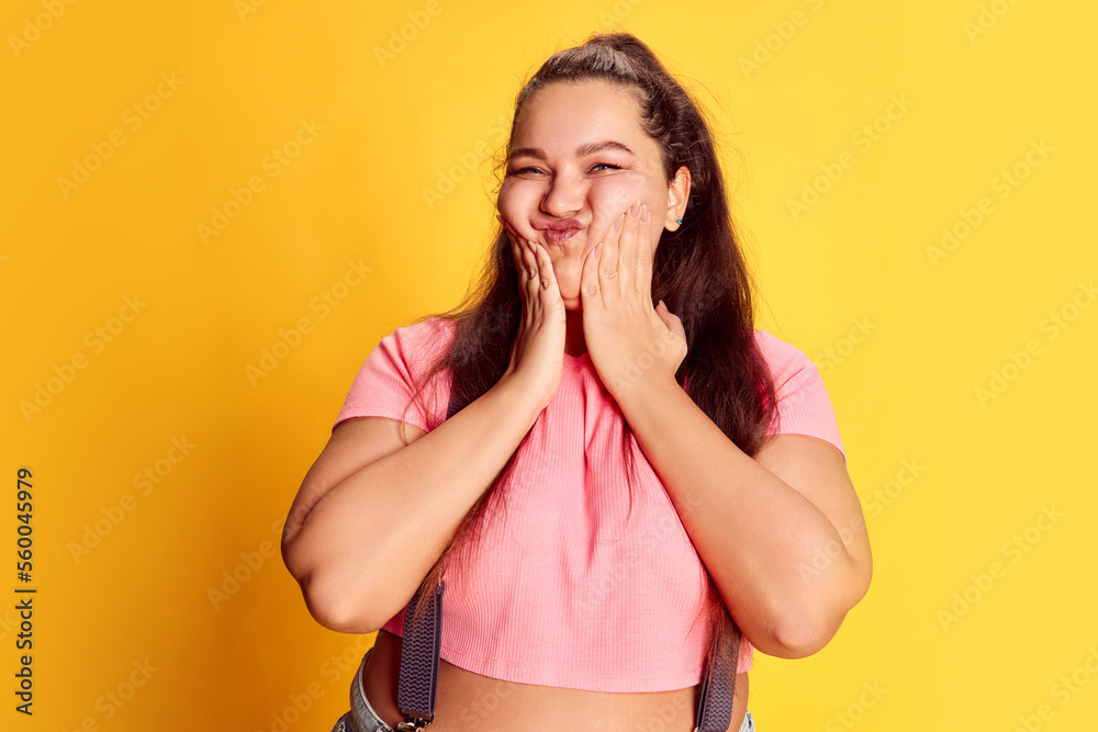 Portrait of young overweight woman in casual bright clothes posing over vivid yellow studio background. Funny face Portrait of young overweight woman in casual bright clothes posing over vivid yellow studio background. Funny face
