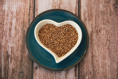 small grains of natural brown buckwheat in a decorative plate in the form of a heart
