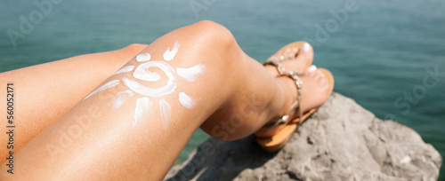 Woman sunbathing on the beach with a drawing of sun on her leg  with cream banner size