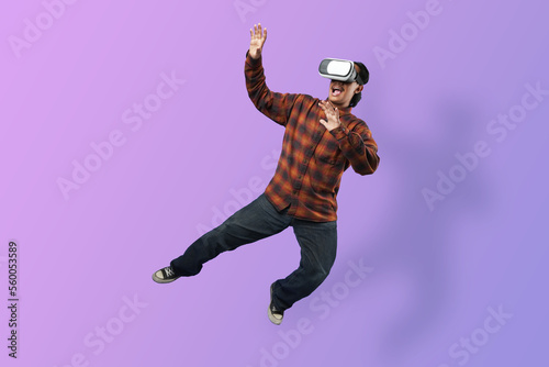 Expression of Amazed young Asian man wearing a VR glass headset levitating in the air on futuristic purple cyberpunk light background