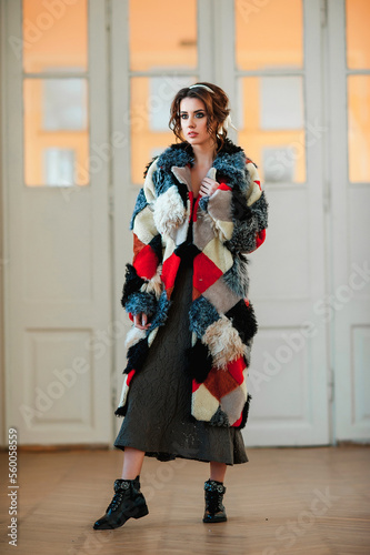  sexy girl dressed in a fur coat and posing indoors on the background of the door; warm long fur coat