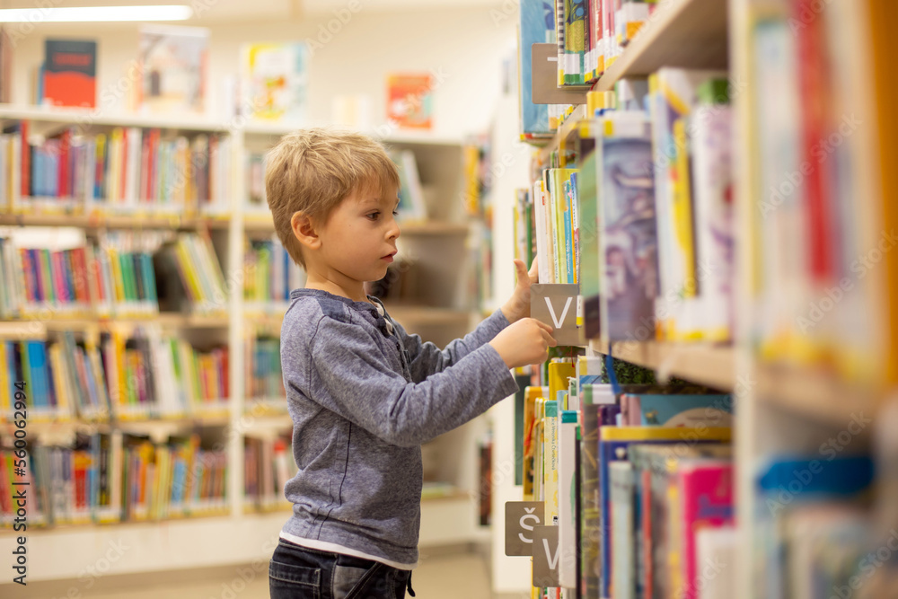 Adorable little boy, sitting in library, reading book and choosing what to lend, kid in book store. Adorable little boy, sitting in library, reading book and choosing what to lend, kid in book store.