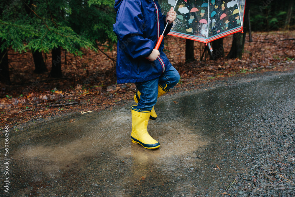 Young child in yellow rain boots stomps in a mud puddle Young child in yellow rain boots stomps in a mud puddle
