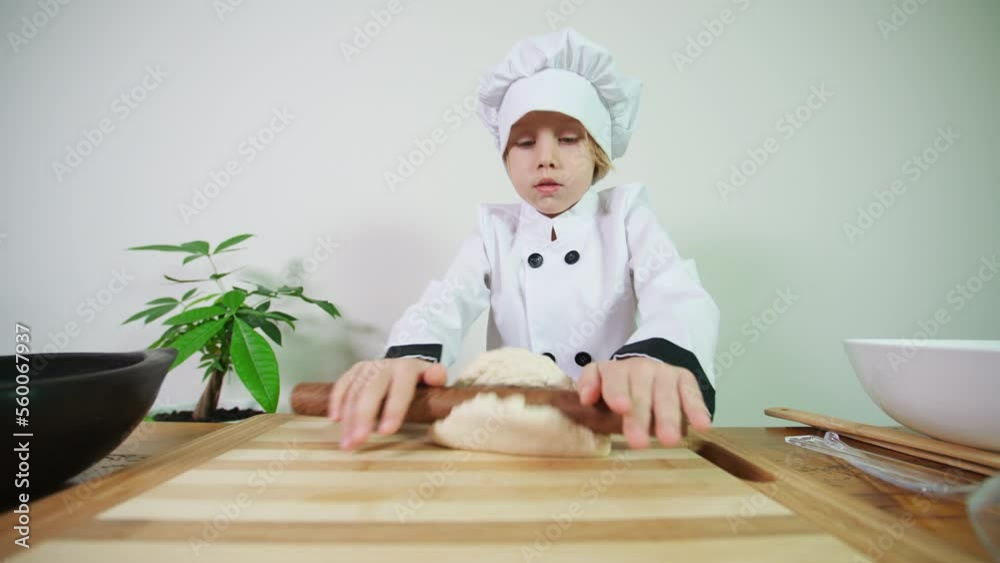 5 years old caucasian boy dressed like a chef rolls out pastry with a rolling pin cooking cookies or a pie or a pizza. A boy prepares dough for baking in the oven 5 years old caucasian boy dressed like a chef rolls out pastry with a rolling pin cooking cookies or a pie or a pizza. A boy prepares dough for baking in the oven