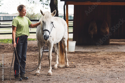 Beautiful white horse and his trainer, a woman standing still inside the fence on a ranch