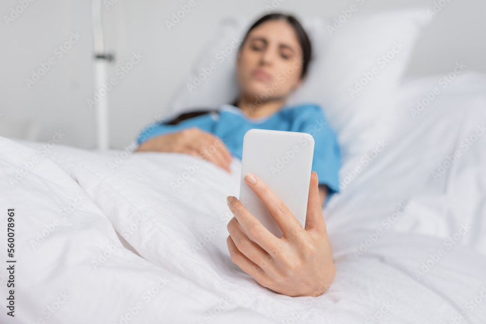 Blurred woman in patient gown using smartphone on bed in clinic. Blurred woman in patient gown using smartphone on bed in clinic.