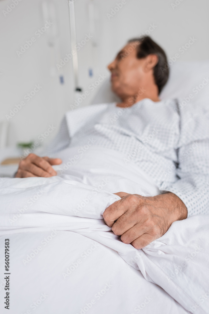 Blurred senior patient touching blanket while lying on bed in hospital. Blurred senior patient touching blanket while lying on bed in hospital.