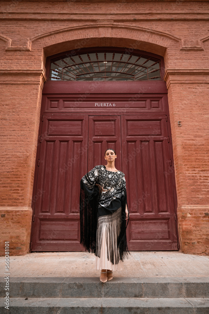 Portrait of a woman wear a spain traditional outfit with a black shawl in front of bullring