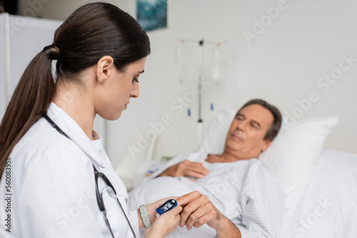 doctor looking at pulse oximeter on finger of senior patient in hospital.