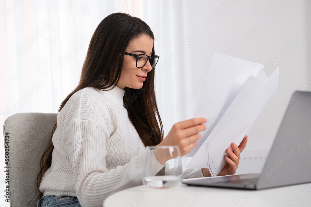 Smiling young businesswoman in glasses looking at the documents and check with notebook. Smiling young businesswoman in glasses looking at the documents and check with notebook.