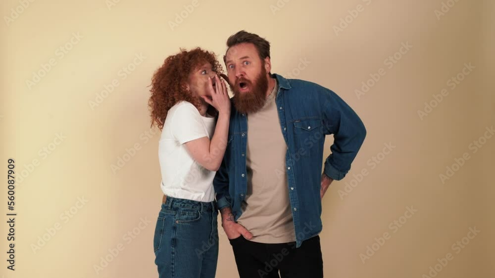 Happy redhaired woman tells a secret in her boyfriend's ear in beige studio Happy redhaired woman tells a secret in her boyfriend's ear in beige studio